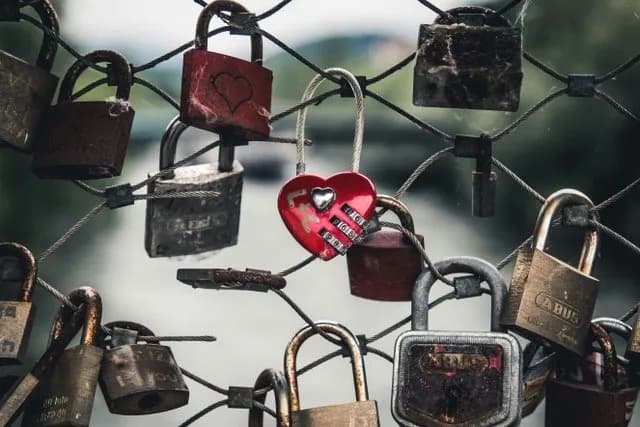 Close-up of love locks fastened to a wire mesh fence, featuring a prominent red heart-shaped padlock.