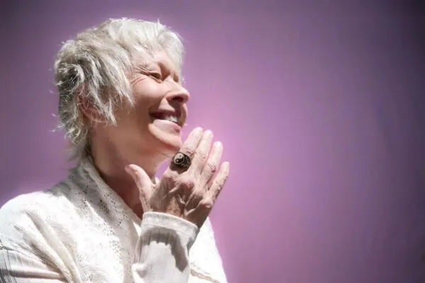 Becca Williams smiling joyfully with short silver hair and her hand near her chin, embodying Aging and Healing against a lavender background.
