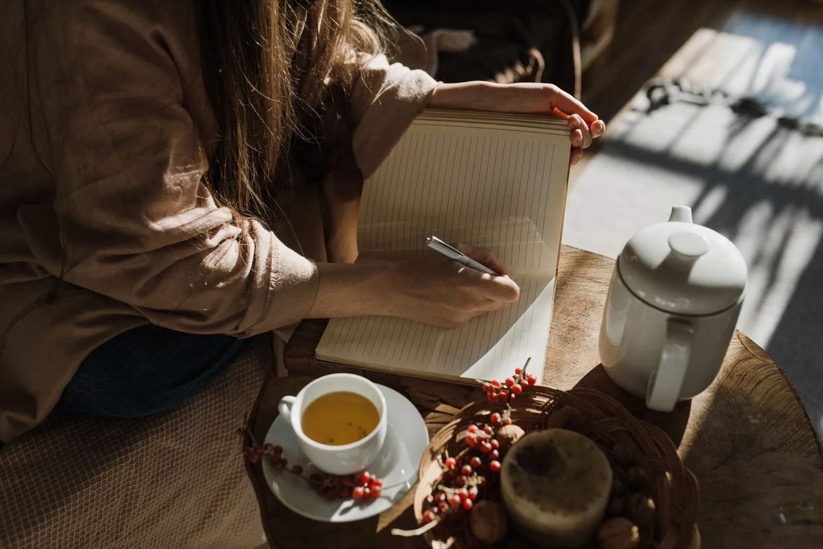 Hands journaling beside a cup of tea in warm light