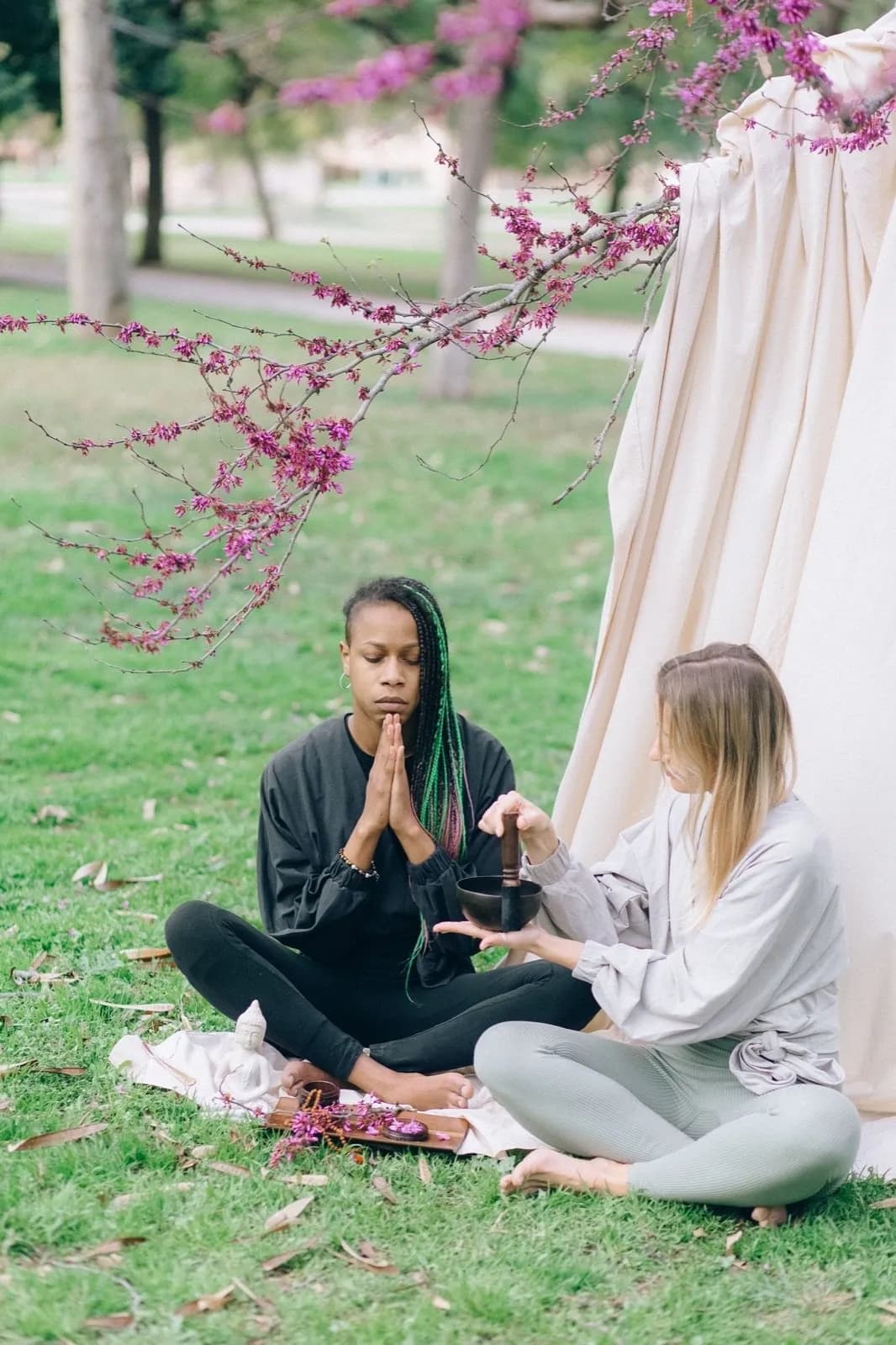 Two people meditating outdoors near a tent with a singing bowl